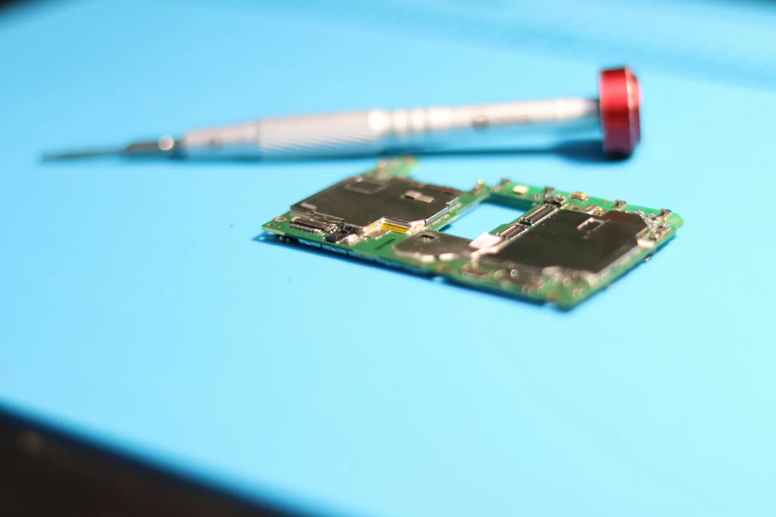 A screwdriver resting on a blue circuit board.