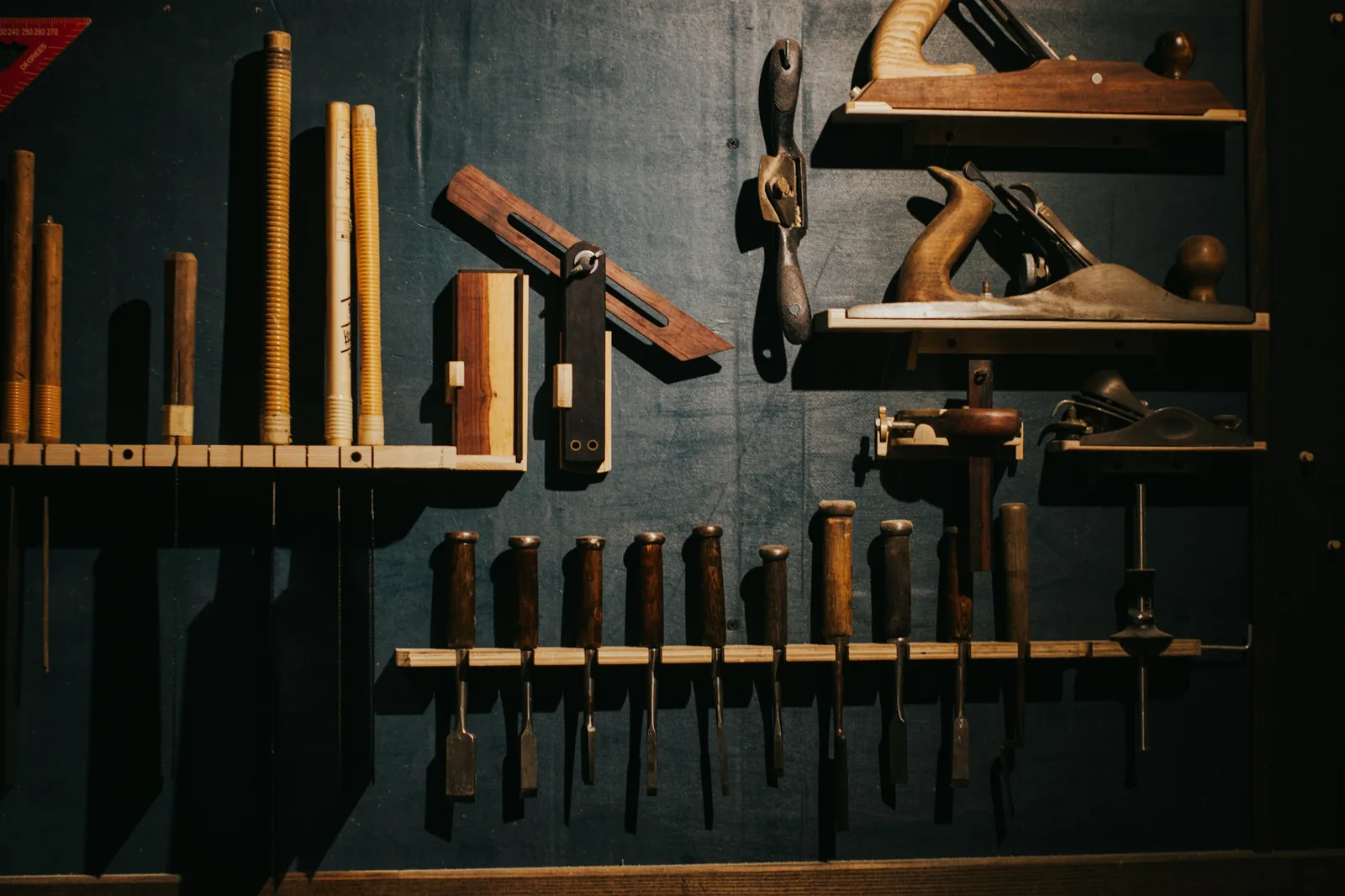 Woodworking hand tools arranged on a dark workshop wall.